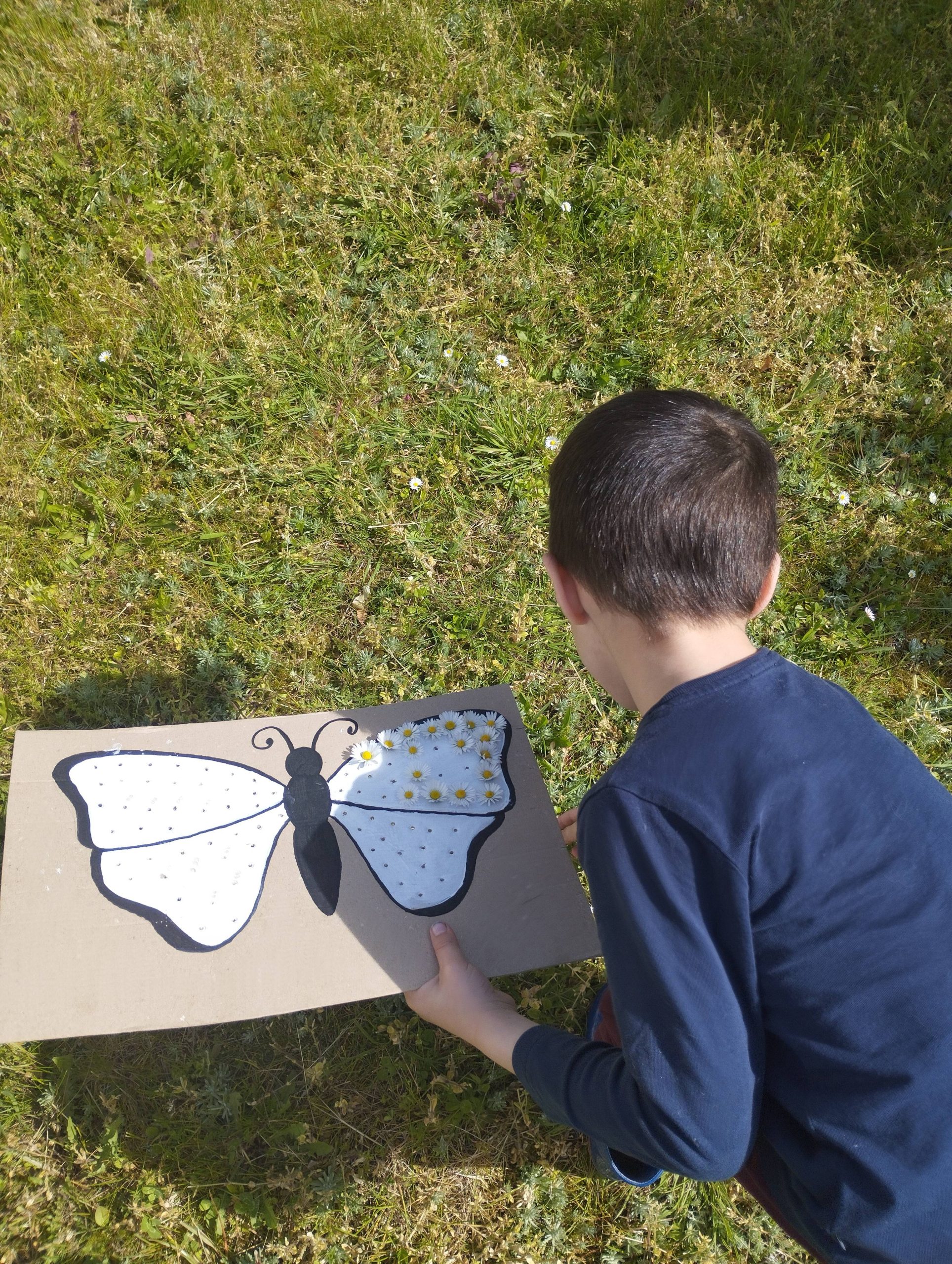 Enfant développant sa motricité fine en insérant des fleurs dans un papillon en carton